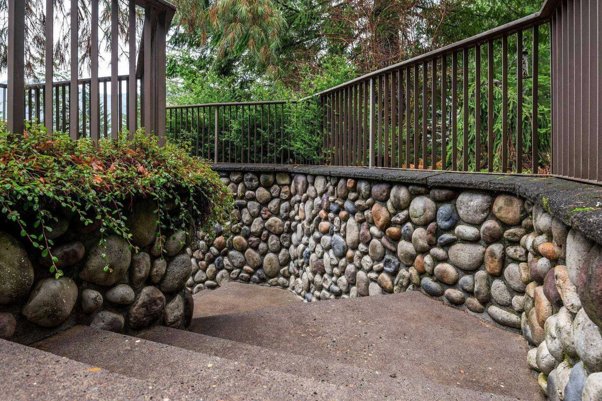 A calming outdoor scene highlights a stone wall, steps, and railing, all surrounded by lush greenery. This tranquil spot offers a quiet place to pause, listen to nature, or watch pets play nearby, reinforcing the property's expansive and peaceful atmosphere.