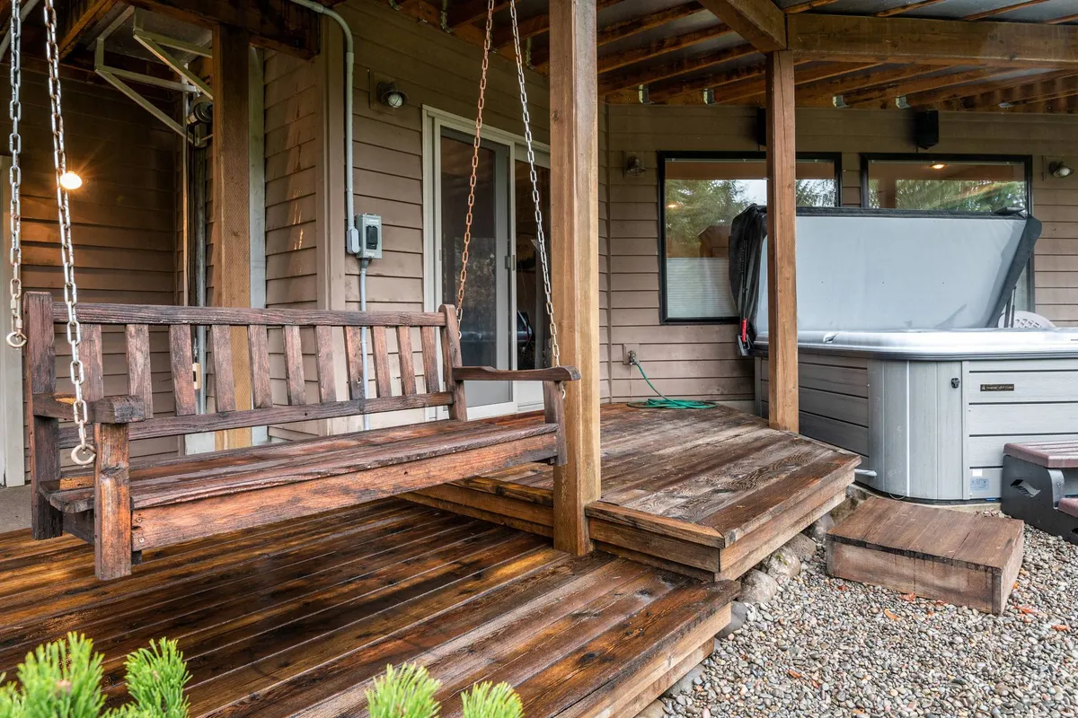 A wooden deck featuring a cozy chain swing and a bubbling hot tub, all set against a backdrop of natural greenery. The space is designed for relaxation, with ample room for socializing or private contemplation.