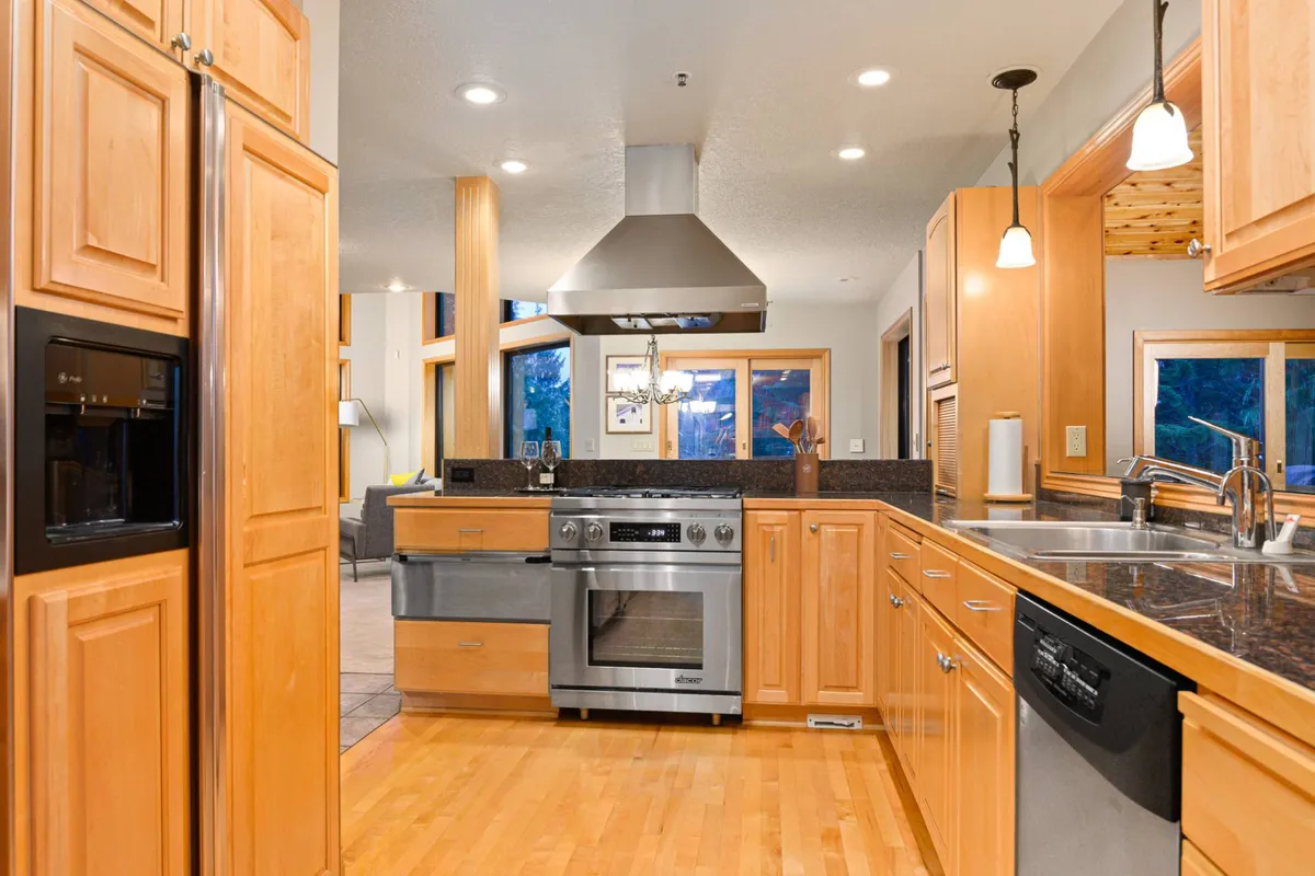 A stylish, open kitchen with a central island, stainless steel appliances, wood cabinetry, and large windows. The space is both functional and welcoming, designed for group cooking, socializing, and seamless connection to adjacent living areas.