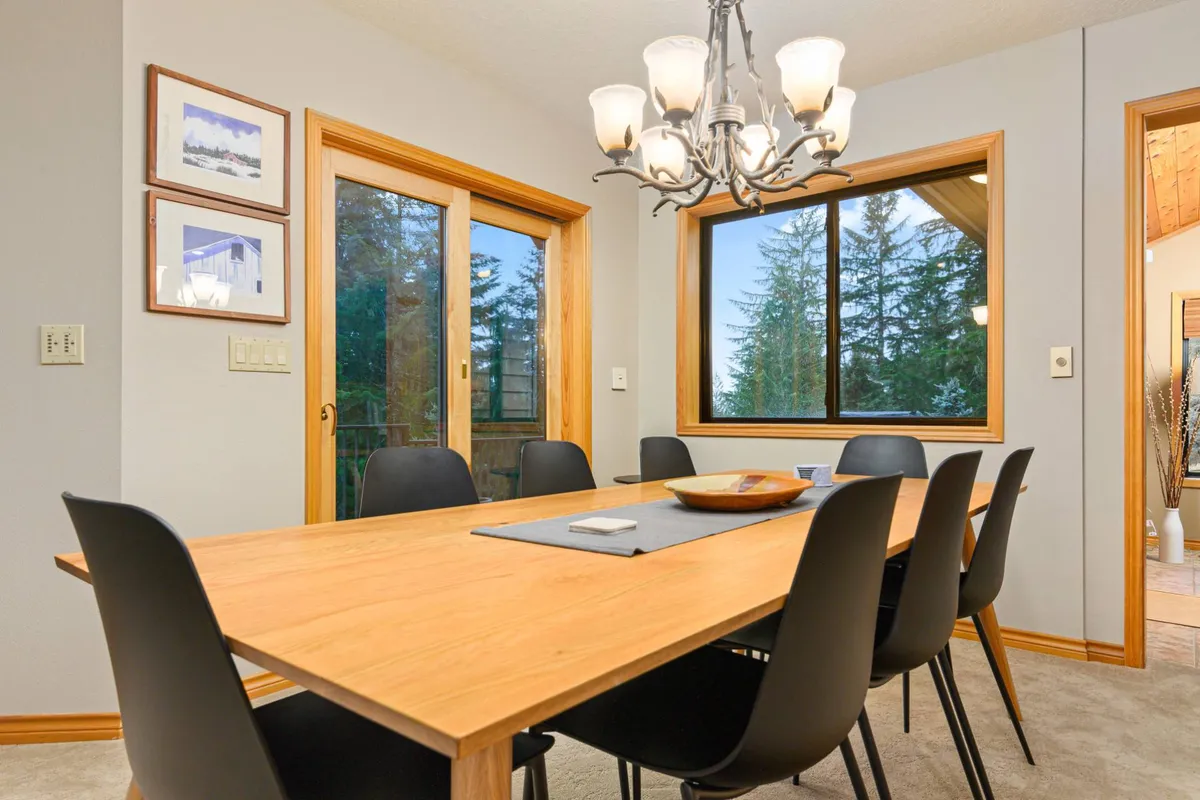 A bright dining area featuring a beautiful table set beneath a chandelier, with windows framing views of the outdoors. The space is arranged for family dinners, celebrations, or quiet moments, reinforcing the sense of shared experiences.