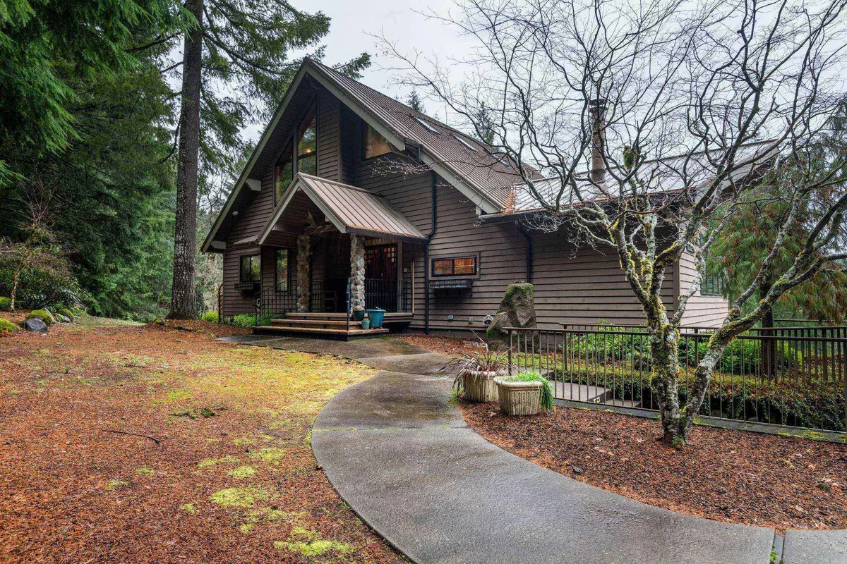 The image features the home's exterior, showcasing the welcoming facade, a winding pathway, and mature trees that envelop the property. The natural surroundings emphasize the sense of open space and privacy, inviting guests and their pets to step outside and explore.