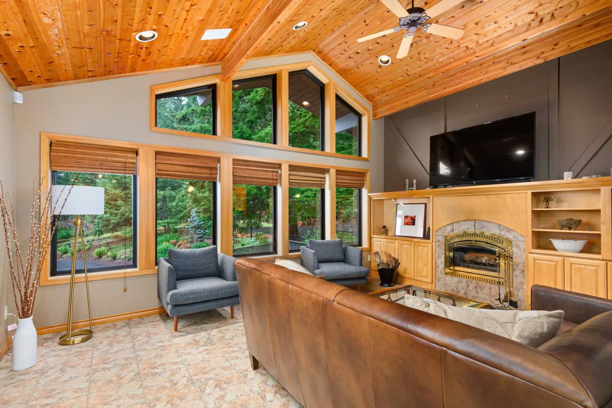 A spacious seating area with large windows overlooking greenery and a fireplace. The room encourages gatherings, with plush seating ideal for group conversations or game nights, and the natural light adds to the inviting atmosphere.
