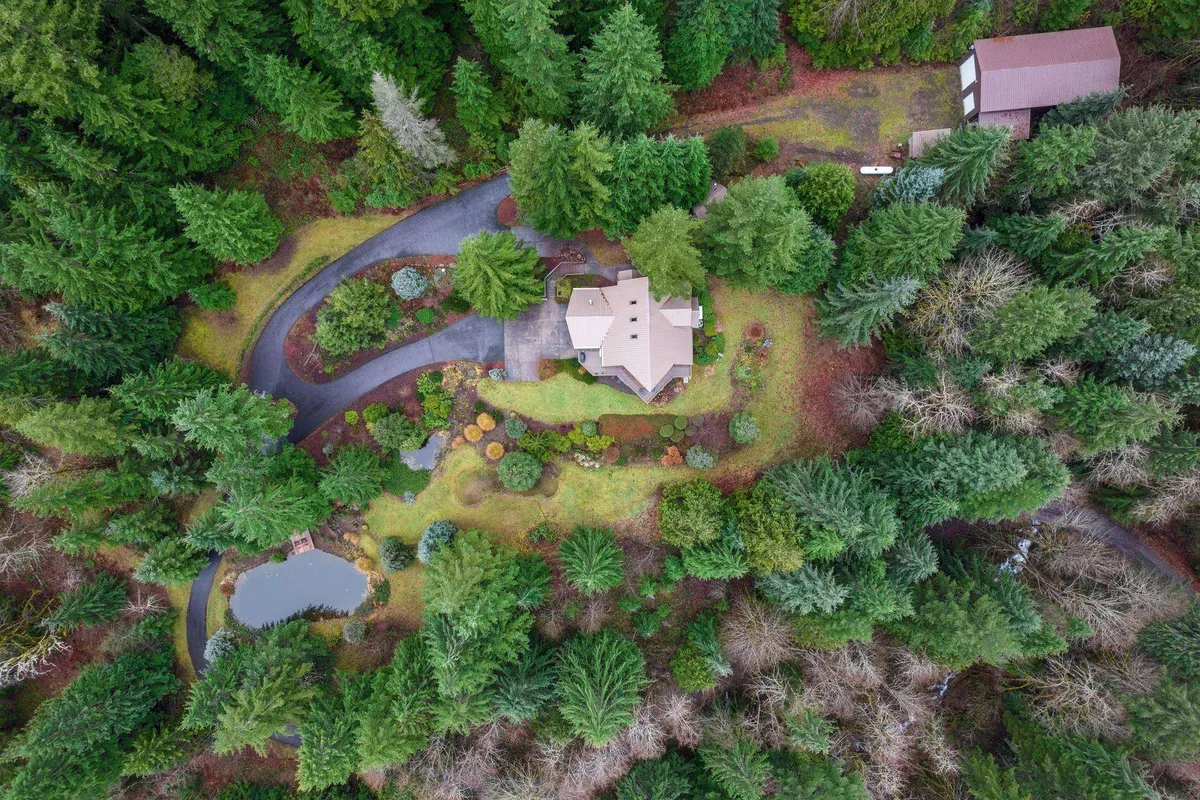 An exterior view of the property surrounded by lush landscaping, a pond, and mature trees, offering a sense of immersion in nature. The inviting house sits in the background, framed by peaceful gardens and an accessible driveway.