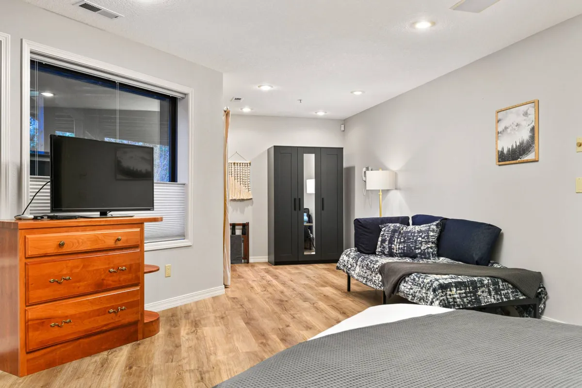 A cozy interior scene with a sofa adorned with decorative cushions, a wooden dresser with a TV, and a wardrobe. The layout is warm and homely, inviting guests to relax, watch TV, or play board games together.