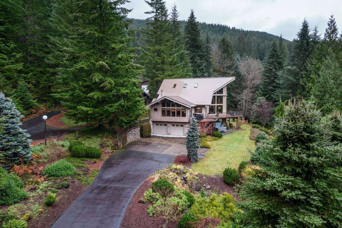 A peaceful exterior shot showing the house set back from the driveway, surrounded by lush greenery and tall trees. The inviting scene suggests a welcoming space for family gatherings, morning coffees on the porch, and evenings under the stars.